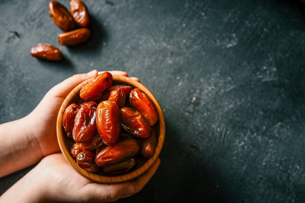Des dattes sucrées dans un bol en bois tenu par les mains sur un fond rustique sombre Une collation saine avec un éclat naturel parfaite pour le régime végétalien du Ramadan ou la cuisine du Moyen-Orient