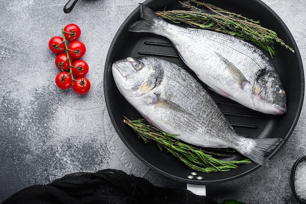 Daurade ou dorado poisson cru sur la lèchefrite avec des ingrédients sur fond texturé blanc gris, espace vue de dessus pour le texte.