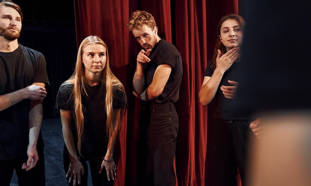 Debout contre des rideaux rouges Groupe d'acteurs vêtus de vêtements de couleur sombre en répétition au théâtre