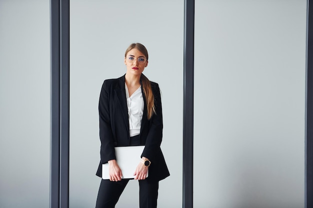 Debout sur fond gris Jeune femme adulte en vêtements formels est à l'intérieur dans le bureau