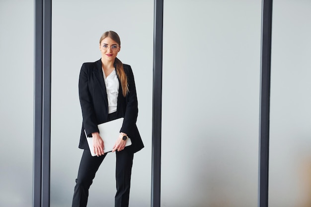 Debout sur fond gris Jeune femme adulte en vêtements formels est à l'intérieur dans le bureau