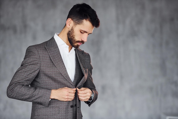 Debout sur fond gris Jeune homme d'affaires élégant en costume à l'intérieur Conception du succès