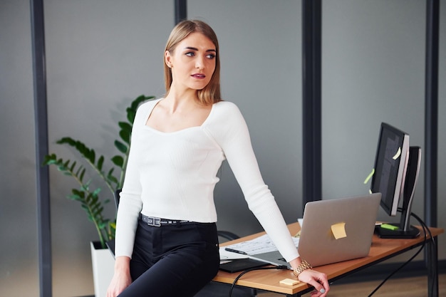 Debout près de la table Jeune femme adulte en vêtements formels est à l'intérieur du bureau