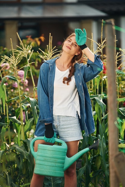 Photo debout et tenant l'arrosage peut belle jeune femme est jardinage