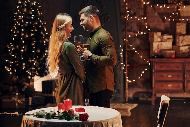 Debout et tenant de grands verres avec du vin Un jeune couple charmant a un dîner romantique à l'intérieur ensemble