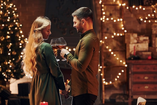 Debout et tenant de grands verres avec du vin Un jeune couple charmant a un dîner romantique à l'intérieur ensemble