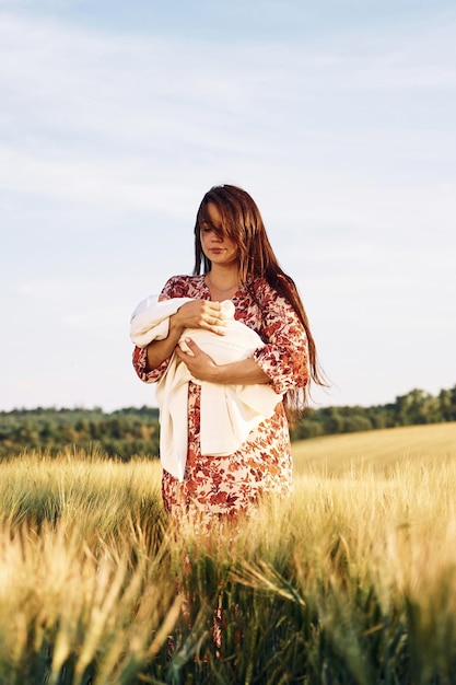 Debout et tenant son bébé nouveau-né Superbe femme est sur le terrain agricole