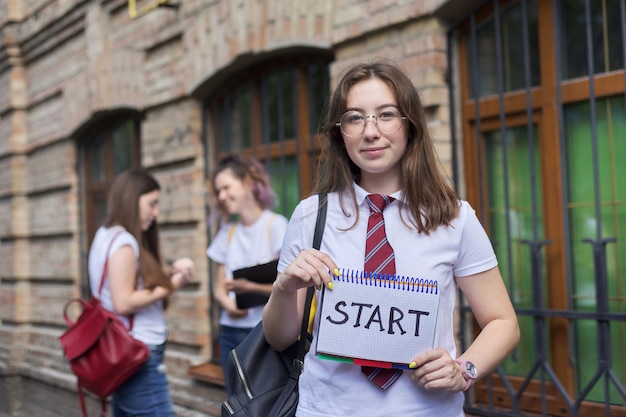 Début. Une étudiante tient un cahier avec un début de mot, début des cours à l'école, à l'université. Construction de briques et fond d'étudiants parlants