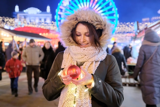 Début de la nouvelle année 2021, femme heureuse montrant une boule de Noël rouge avec texte 2021 au marché de Noël