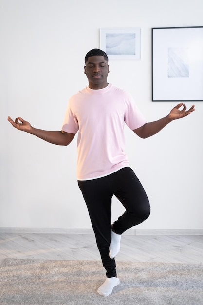 Début de la pratique du yoga Homme noir Formation à domicile Première leçon Trouver l'harmonie Homme africain méditant essayant de rester arbre pose une jambe mains zen intérieur de la pièce lumineuse