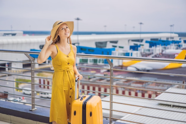 Début de son voyage Belle jeune femme ltraveler dans une robe jaune et une valise jaune attend son vol
