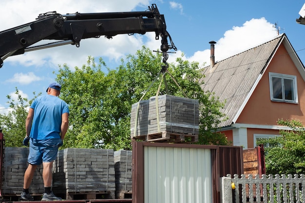 Déchargement de dalles de pavage d'un camion Des hommes déchargent des dalles de pavage à l'aide d'un manipulateur Des ouvriers déchargent des matériaux de construction d'une grosse machine