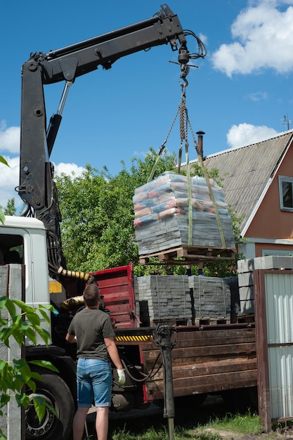 Déchargement de dalles de pavage d'un camion Des hommes déchargent des dalles de pavage à l'aide d'un manipulateur Des ouvriers déchargent des matériaux de construction d'une grosse machine