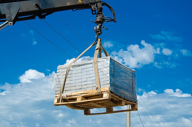 Déchargement de dalles de pavage d'un camion. Des hommes déchargent des dalles de pavage à l'aide d'un manipulateur. Les travailleurs déchargent les matériaux de construction d'une grosse machine.