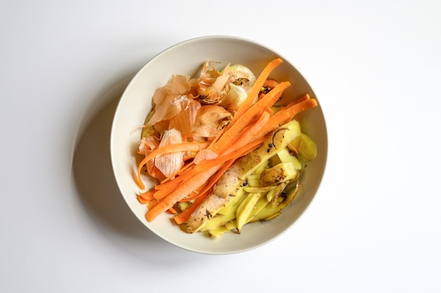 Déchets alimentaires de la cuisine domestique, nettoyage des légumes oignons pommes de terre et carottes dans une assiette sur un tableau blanc. tri des déchets alimentaires ménagers