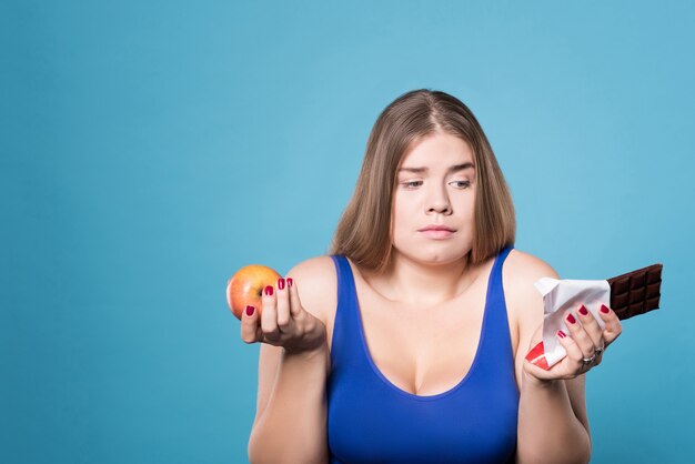 Photo décision difficile. portrait de jeune femme assez douteuse tenant la pomme dans une main et le chocolat dans une autre.