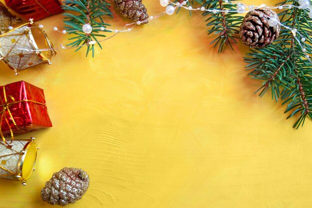 Photo le décor du nouvel an sur une table jaune, des branches de sapin, des cônes dorés de paillettes, des guirlandes et des jouets de noël.