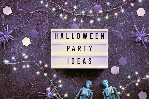 Décor d'Halloween et idées de fête d'Halloween écrites sur la zone de texte Fond minimal d'Halloween avec des squelettes vert pâle et des araignées violettes Fond sombre avec des hexagones en papier et des lumières sur la guirlande