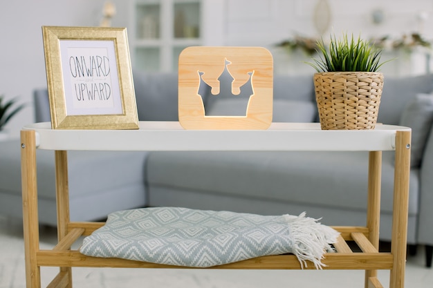 Décor à la maison, lampe en bois. Vue de face de la petite table avec cadre photo, lampe en bois décorative avec photo de la tour du château et plante verte en pot de fleur en osier.