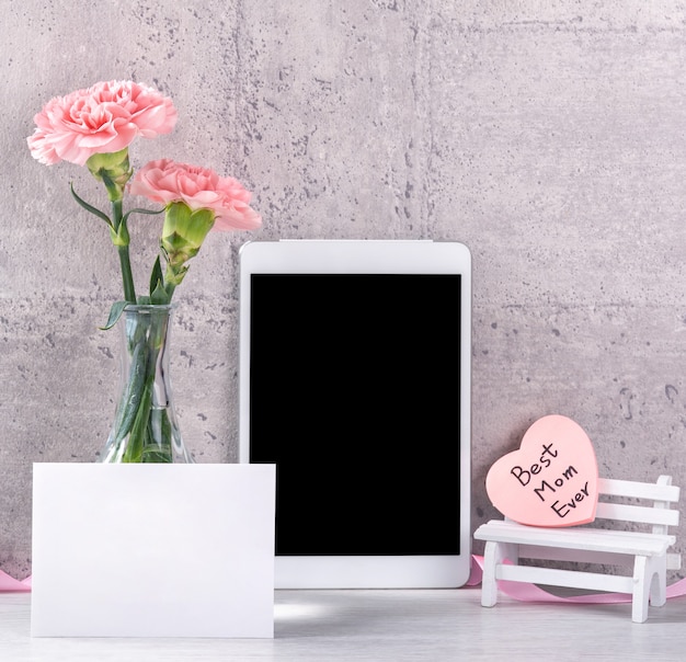 Décor à la maison avec œillet en fleurs et tablette comme cadre photo à côté du mur sur la table