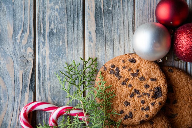 Décor de Noël festif. boules de canne en bonbon biscuits aux pépites de chocolat et brindille de genévrier sur fond de bois rustique.