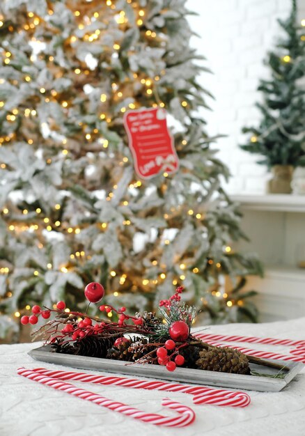 Décor de Noël sous la forme d'une branche artificielle avec des baies rouges et des cônes sur un plateau sur le lit sur fond de lumières de Noël