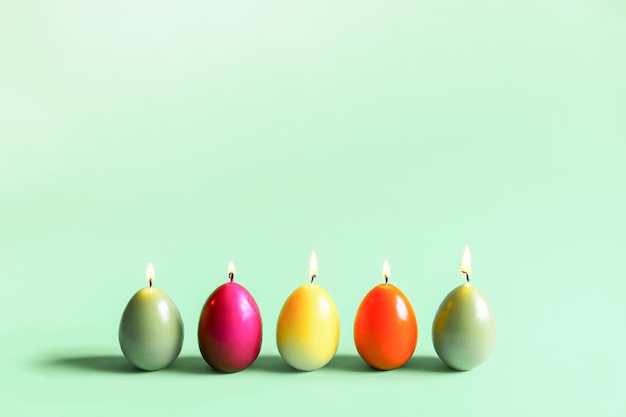 Décor traditionnel de Pâques. Bougies de paraffine brûlantes lumineuses en forme d'oeufs colorés sur fond vert.