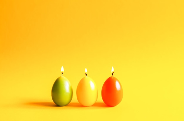 Décor traditionnel de Pâques. Groupe de bougies de paraffine brûlantes lumineuses en forme d'œufs colorés sur fond jaune chaud et doux.