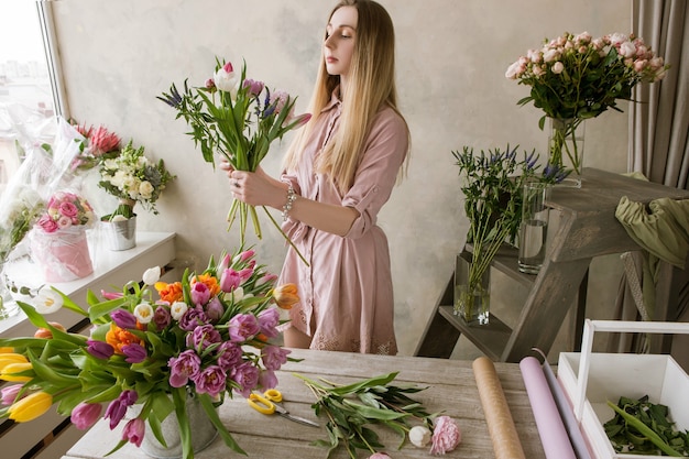 Un décorateur fleuriste professionnel dans un magasin de fleurs compose un nouveau bouquet. Travail de femme avec assortiment de tulipes, lieu de travail d'artiste