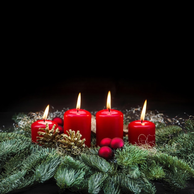 Décoration de l'Avent quatre bougies allumées rouges et branches d'arbres de Noël sur fond noir