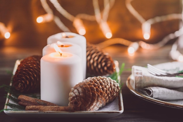 Décoration confortable d'hiver avec des bougies allumées blanches sur une table de fête en bois et des lumières floues sur un fond