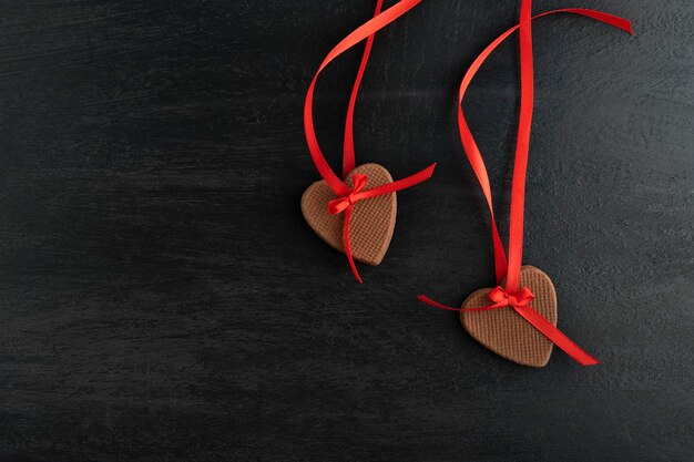 Décoration de deux biscuits au gingembre le jour de la Saint-Valentin. Biscuits en forme de coeur avec des rubans rouges sur une surface noire.