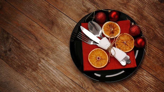 Décoration de dîner de Noël avec des oranges séchées et une serviette rouge sur une plaque noire sur fond de bois. Espace pour le texte