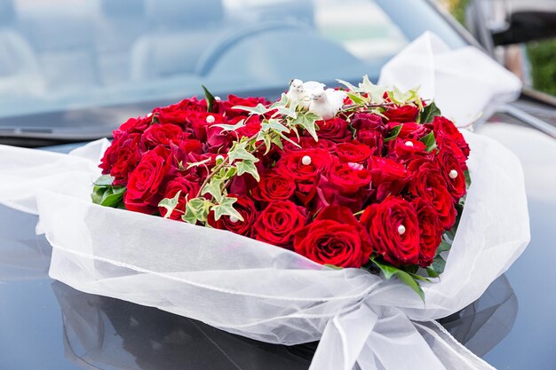 Photo une décoration élégante de fleurs roses rouges, rubans sur une voiture de mariage noire brillante