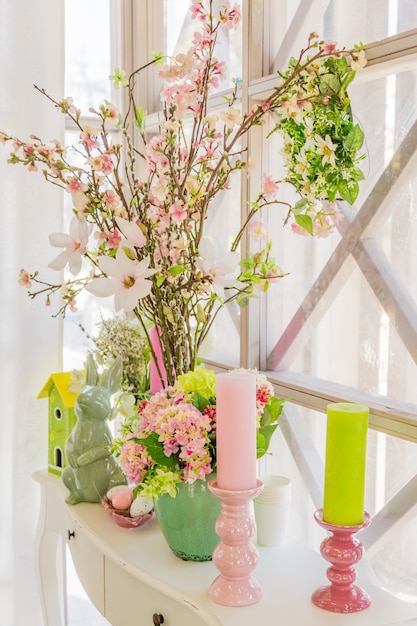 Photo décoration intérieure de pâques. composition beatuful avec des bougies. oeufs, lapin, maison d'oiseaux et branches de pomme en fleurs.