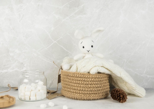 Décoration de maison de Noël Le lièvre jouet blanc à tricoter est sur un panier à tricoter avec Marchmelloy sur fond gris