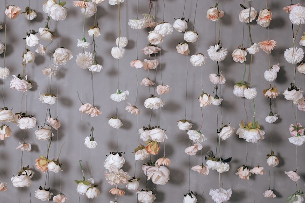 Décoration de mariage avec de nombreuses fleurs artificielles accrochées au mur gris.