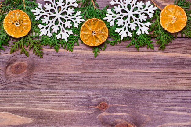 Décoration de Noël avec des branches de thuya, des flocons de neige et des mandarines sur une table en bois.