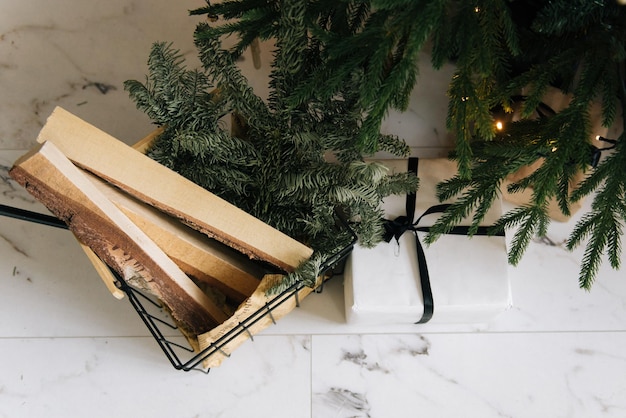 Décoration de Noël cadeaux joliment emballés sous le sapin de Noël avec du bois de chauffage pour la cheminée