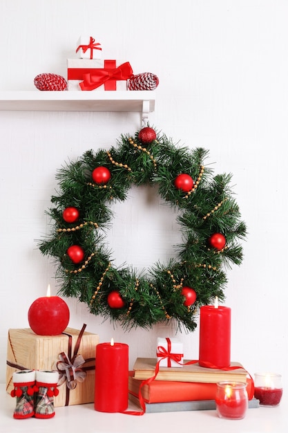 Décoration de Noël avec couronne, bougies et coffrets cadeaux sur étagère sur fond de mur blanc