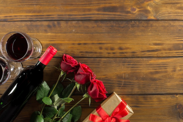 Décoration romantique Saint Valentin avec roses, vin et coffret cadeau sur une table en bois marron