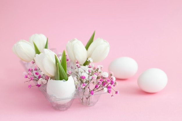 Photo décoration de vacances de pâques en tulipes blanches coquille d'oeuf et gypsophile rose et deux oeufs blancs sur fond pastel rose. copie espace.