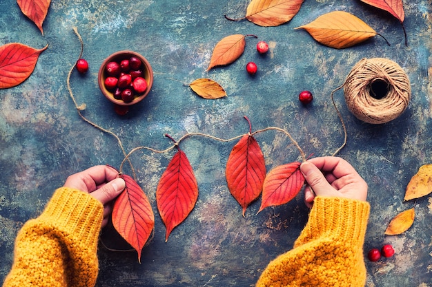 Photo décorations de bricolage d'automne à partir de matériaux naturels. faire une guirlande avec un cordon de chanvre et des feuilles d'automne rouge vif.