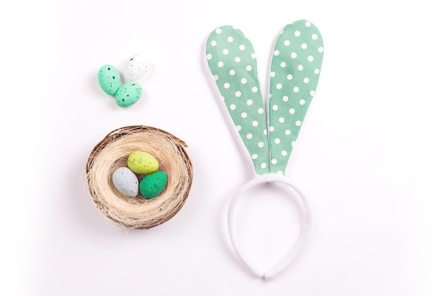 Photo décorations colorées avec nid d'oeufs de pâques et oreilles de lapin sur fond blanc. espace de copie, vue de dessus