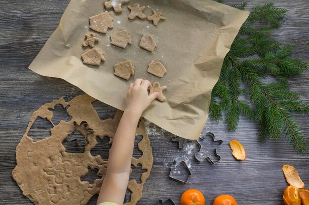 Décorations du Nouvel An et de Noël sur une surface en bois avec des mandarines et un arbre de Noël Un petit enfant met des biscuits au gingembre sous forme d'hommes et une maison sur une plaque à pâtisserie