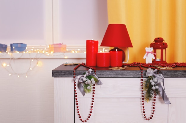 Décorations de Noël colorées et bougies sur la table contre la fenêtre décorée de lumières rougeoyantes, gros plan