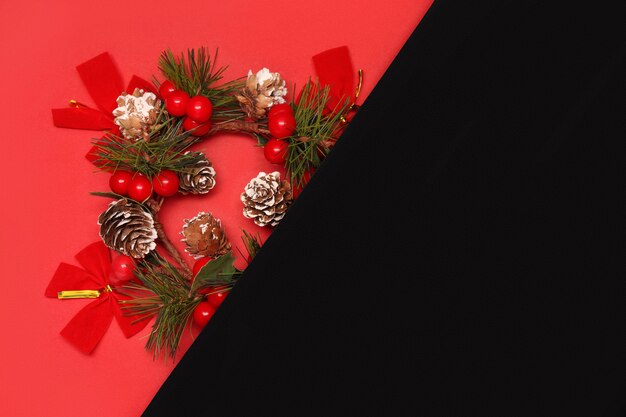 Décorations de Noël, cône, branche de sapin et arcs sur fond rouge avec feuille blanche en papier noir à droite. Carte de Noël ou du nouvel an, espace de copie.