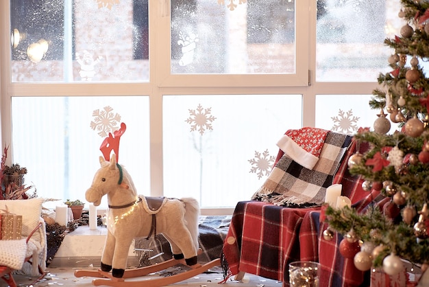 Décorations de Noël confortables pour la maison Canapé confortable avec plaid et chaise berçante à cheval avec arbre de Noël décoré avec des cadeaux près de la fenêtre