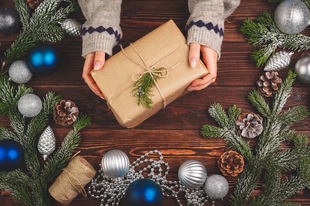 Décorations de Noël sur une table en bois avec un cadeau décoré dans les mains de la femme