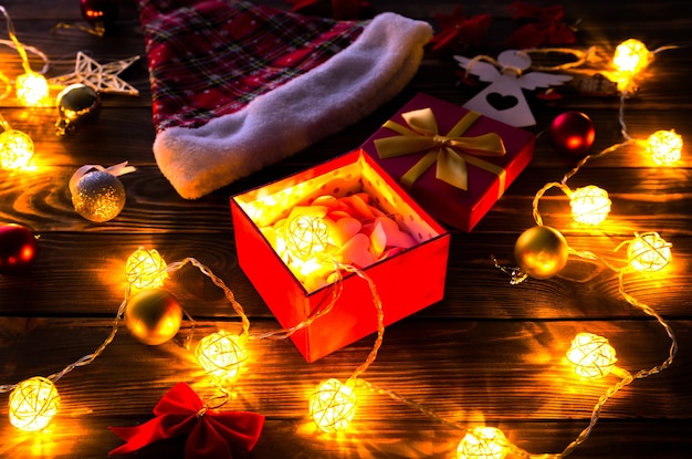 Décorations de Noël sur la table en bois. Lumières, boules et bonnet de Noel. Ambiance romantique du soir. Ambiance chaleureuse. Vacances à plat. Notion festive. Nouvel an 2021.